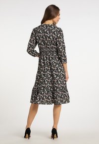 Rochie neagră cu flori, cu talie elastică, mânici lungi și fustă evazată. Prezintă flori mici roz și albe pe un fundal închis.