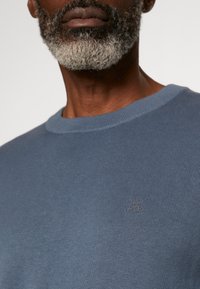 Maglione a costine azzurro chiaro con collo a giro, caratterizzato da un sottile dettaglio del logo sul petto e una superficie liscia.