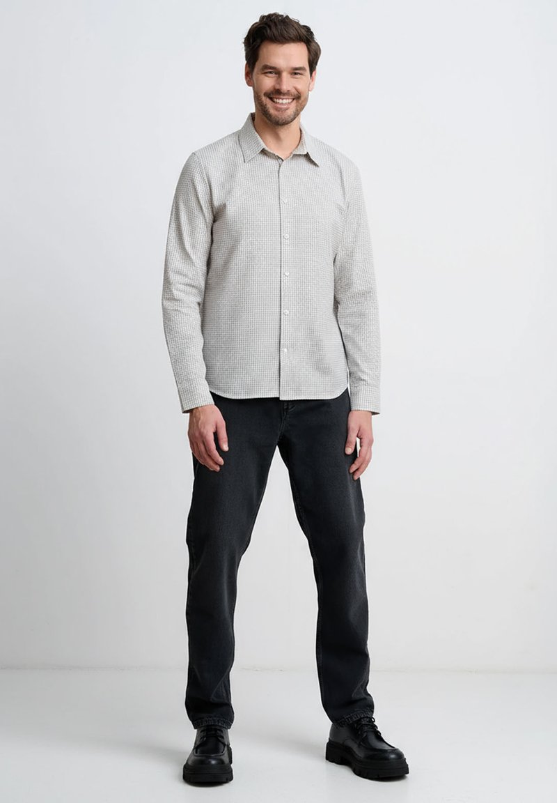 Jasnoszara koszula zapinana na guziki z wzorem w kratę, długimi rękawami i spiczastym kołnierzykiem, w połączeniu z ciemnymi dżinsami i czarnymi butami.