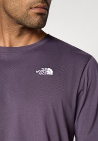 Ανδρικό μωβ μπλουζάκι με στρογγυλή λαιμόκοψη και κοντά μανίκια, με λευκό κεντημένο λογότυπο στην αριστερή πλευρά του στήθους. Λείο ύφασμα.