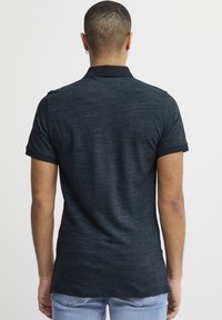 Polo shirt pour homme de couleur gris foncé à manches courtes, avec une bordure de col noire et un tissu texturé. Il présente une étiquette sur la couture latérale et une coupe décontractée.