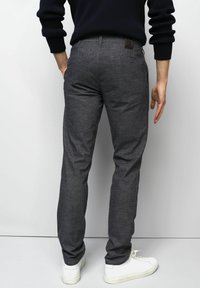 Graue Baumwollhose mit feiner Struktur, schmaler Schnitt und hinteren Taschen, kombiniert mit weißen Sneakers. Der Bund ist mit einem braunen Etikett versehen.