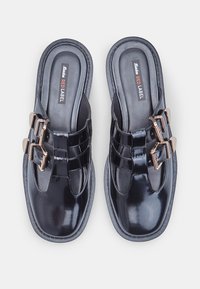 Black patent leather slip-on shoes with dual gold buckles, curved design, cushioned footbed, and textured rubber sole.