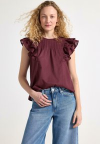 Burgundské tričko s krátkým rukávem a volánky, s plisé vzhledem, zkombinované s jasně modrými širokými džíny. Jednoduchý a moderní design.