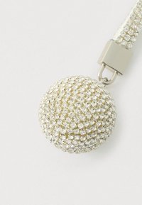 Apvalus, krištolu inkrustuotas pakabutis sidabro atspalvių, su lygiu blizgiu paviršiumi, pritvirtintas prie metalinės sagties saugiam tvirtinimui.