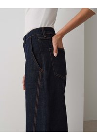 Dark blue high-waisted jeans with a fitted silhouette, featuring orange stitching and side pockets. Fabric shows denim texture and depth.