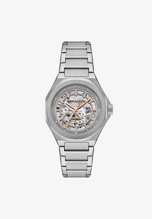 Sølv rustfrit stål ur med et skeletdials, der har orange accenter og et børstet metalarmbånd. Automatisk bevægelse synlig gennem urskiven.