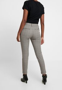 Haut noir à manches courtes associé à un pantalon à taille haute en motif pied-de-poule avec des fentes latérales et des bottines noires.