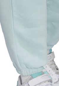 Jasnoniebieskie dresy z wykończonymi nogawkami, w zestawie z białymi i jasnoniebieskimi butami Adidas oraz białymi skarpetkami.