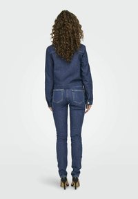 Giacca di denim e jeans aderenti di un blu scuro. La giacca presenta un design accorciato e maniche lunghe; i jeans hanno tasche posteriori e una vestibilità slim.
