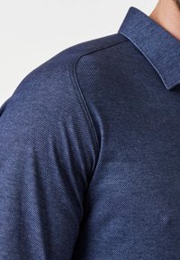 Marineblauwe polo shirt met een gestructureerde, ribbelstof. Het heeft een klassieke kraag en korte mouwen, met een getailleerd ontwerp en subtiele glans.