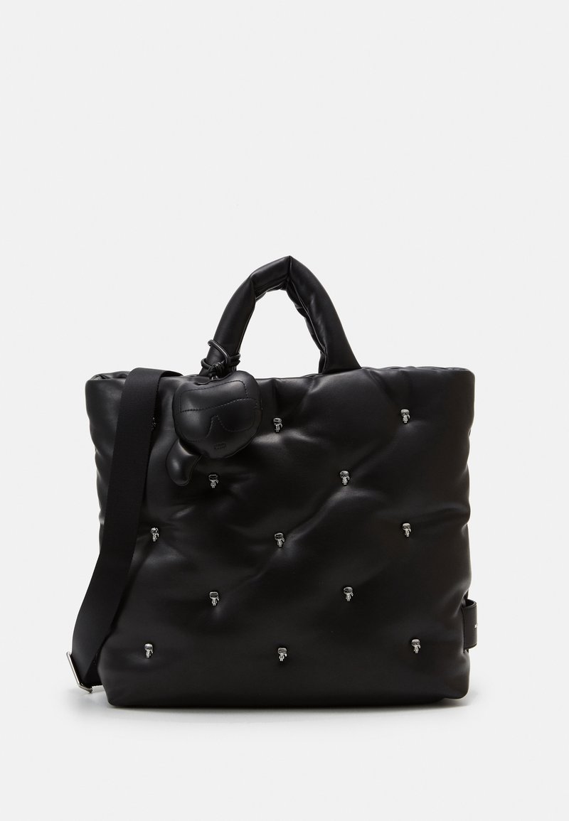 Sac cabas matelassé noir avec de petites clous argentés, une anse épaisse, une bandoulière ajustable et un charm en forme de cœur attaché à la anse.