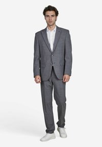 Grijze pak met een gestructureerde pasvorm, voorzien van een notch lapel en een sluiting met twee knopen. Gecombineerd met een witte shirt en witte sneakers.