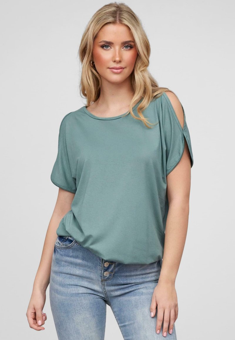 Haut doux à manches courtes en teal avec découpes aux épaules, col rond et coupe ample. Associé à un jean taille haute bleu clair.