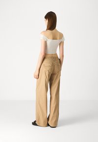 Balta off-shoulder palaidinė su ruffle rankovėmis, derinama su smėlio spalvos plačiomis kelnėmis, turinčiomis dvi užpakalines kišenes ir laisvu siluetu.