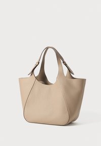 Beige leather tote bag with soft texture, curved shape, and open top. Features two handles and subtle seam detailing on the sides.