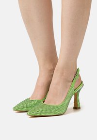 Sapatos de salto alto em verde, com apontados, tipo slingback, adornados com strass. A superfície texturizada e o salto transparente e esbelto criam um design ousado.