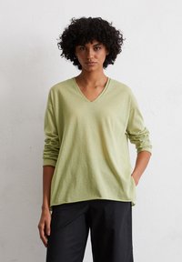 Maglione verde chiaro, a vestibilità ampia, con scollatura a V e maniche lunghe; texture morbida; abbinato a pantaloni neri. Senza fantasie o dettagli aggiuntivi.