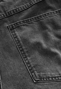 Gros plan sur un tissu en denim noir délavé avec une couture détaillée et une poche arrière rectangulaire.