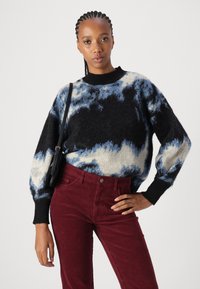 Pletený svetr s černoblue a krémovým tie-dye vzorem; má vysoký límec a objemové rukávy, spárovaný s burgundskými manšestrovými kalhotami.