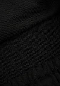 Zbliżenie czarnego materiału ukazujące prążkowane i teksturowane wzory dzianiny z zagiętymi i zebranymi sekcjami.