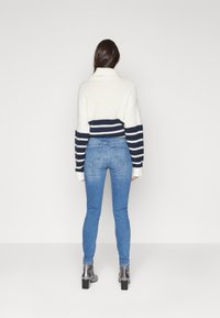 Suéter a rayas blancas y marinas con cuello alto, combinado con jeans ajustados azules y botas tobilleras grises. Textura suave y diseño casual.