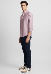 Camisa de mangas largas color rosa claro con diseño de botones, combinada con pantalones azul marino y zapatillas multicolores con un logo azul en el costado.