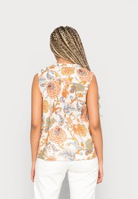 Blouse sans manches à fleurs couleur crème avec des motifs orange, bleu et vert. Tissu doux avec une coupe décontractée et un détail plissé au dos.