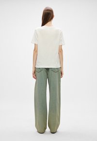 Biela bavlnená tričko s krátkymi rukávmi skombinované s voľnými svetlozelenými džínsy s bočnými vreckami a širokým strihom.