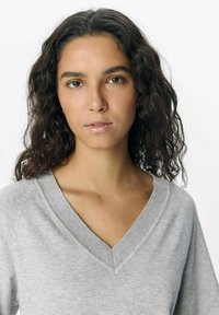 Grå V-hals sweater med ribbet tekstur, der har en afslappet pasform og faldne skuldre. Enkel design uden synlige mønstre eller accenter.