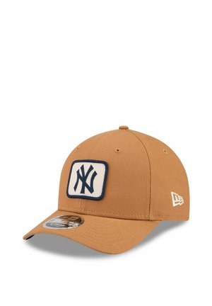 Tan six-panel baseball cap with a navy and white New York Yankees logo patch on front and a small white New Era logo embroidered on the side.