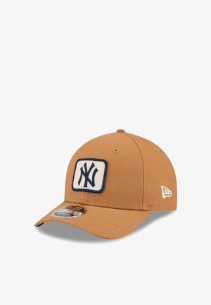 Tan six-panel baseball cap with a navy and white New York Yankees logo patch on front and a small white New Era logo embroidered on the side.
