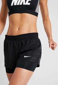 Svarta atletiska shorts med elastisk midja, med en Nike-logotyp på vänster sida och ett åtsittande inre lager för extra stöd.