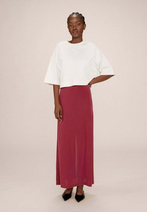 Haut court blanc à manches larges associé à une longue jupe bourgogne. La jupe a une texture lisse, et des escarpins noirs à bout pointu complètent le look.