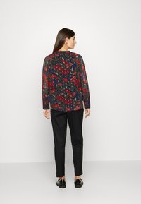 Blusa floral com base azul-marinho, apresentando rosas vermelhas e folhas verdes. Combinada com calças e sapatos pretos, vista de costas.