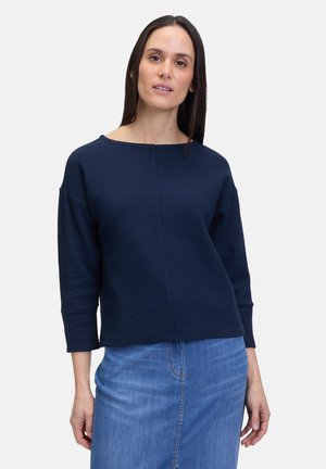 Navy blue knit sweater with a wide neckline, three-quarter sleeves, and a textured pattern. Paired with a denim skirt.