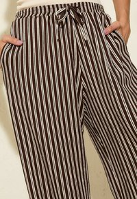 Pantalones a rayas marrón y blanco con cintura ajustable, bolsillos laterales y diseño de pierna ancha, que presentan una tela texturizada.