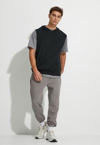 Czarna bezrękawnikowa bluza oversize na szarym t-shircie z krótkim rękawem, w połączeniu z szarymi joggerami z paskami po bokach, uzupełniona białymi trampkami.