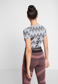 Top de manga corta con estampado en blanco y negro y diseño ajustado. La modelo lleva leggings de cintura alta en color granate con formas abstractas.