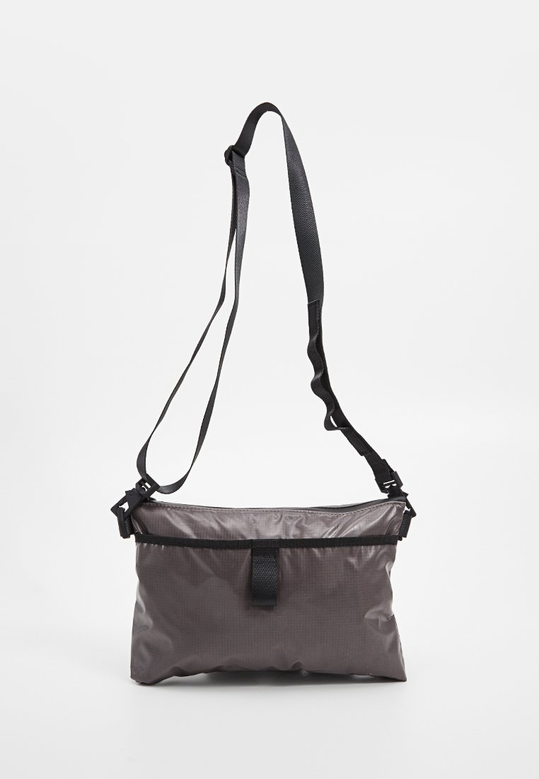 Grau nylon Crossbody-Tasche mit verstellbarem schwarzen Riemen, Reißverschluss und Schleifenverschluss. Sie zeichnet sich durch eine glatte Oberfläche und ein minimalistisches Design aus.