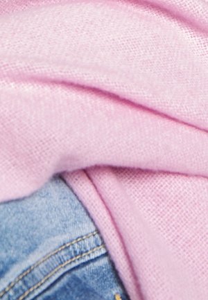 Tissu rose doux recouvre partiellement un jean en denim bleu avec des coutures visibles, mettant en avant des textures et des couleurs contrastées.