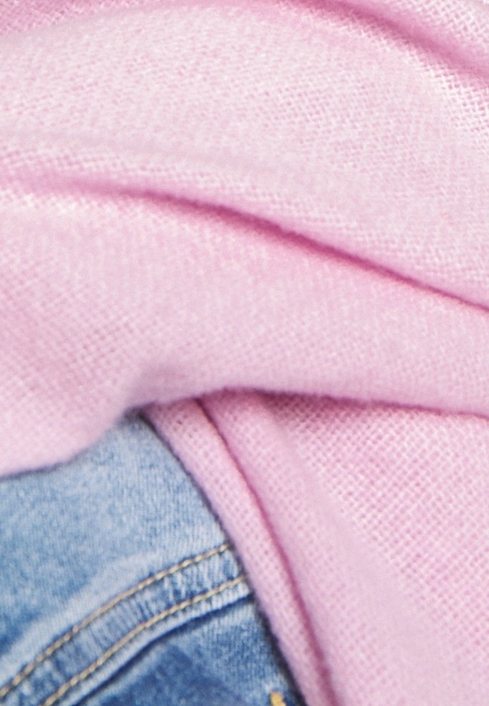 Tissu rose doux recouvre partiellement un jean en denim bleu avec des coutures visibles, mettant en avant des textures et des couleurs contrastées.