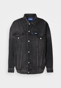 Chaqueta de mezclilla negra con cierre de botones al frente, cuello clásico, dos bolsillos en el pecho y una pequeña etiqueta con logo azul en el pecho izquierdo.