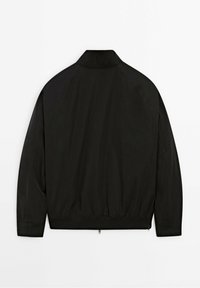 Veste noire à manches longues avec col montant, taille élastique et fermeture éclair, vue de dos sur fond blanc.