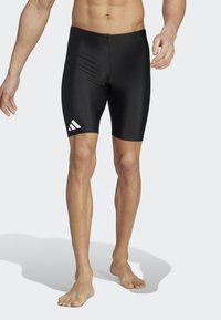 Shorts de bain noirs au design ajusté, fabriqués en matériau lisse. Présente un logo Adidas blanc sur le côté gauche.