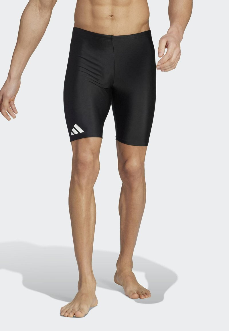 Shorts de bain noirs au design ajusté, fabriqués en matériau lisse. Présente un logo Adidas blanc sur le côté gauche.