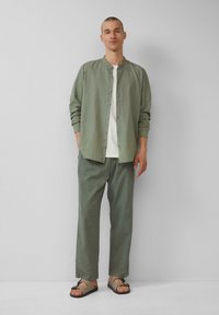 Chemise boutonnée vert clair, t-shirt blanc en dessous, pantalon assorti vert clair, associé à des sandales marron. Design épuré et décontracté.