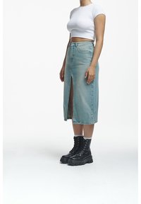 Light blue denim skirt with a front slit, paired with black lace-up combat boots. Model wears a fitted white crop top.