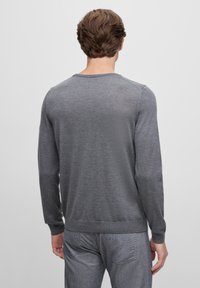 Grauer Langarmpullover mit rundem Halsausschnitt, weicher Textur und engen Bündchen, kombiniert mit grauen Textilhosen. Rückansicht.