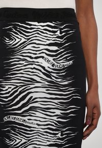 Črna krila z belim vzorcem zebre, narejena iz fleksibilnega materiala. Pas ima vtisnjen napis "Versace Jeans Couture".
